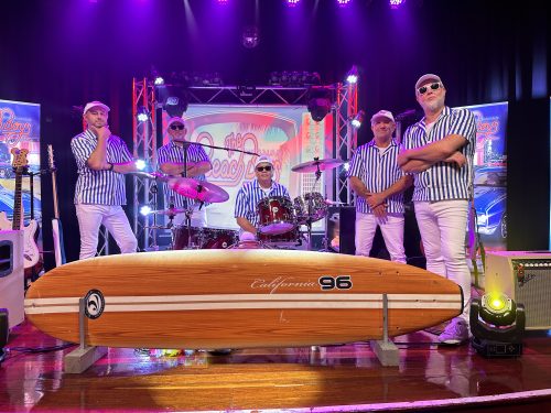 the australian beach boys standing on stage with a surfboard
